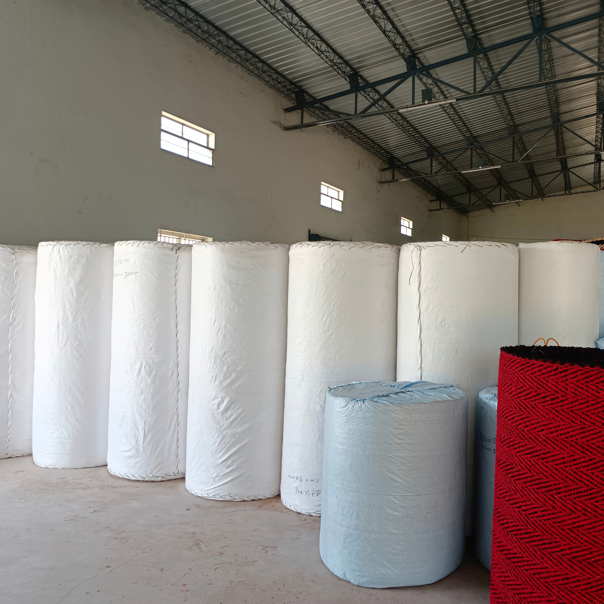 Coir matting rolls wrapped in white protective covering and stacked in the warehouse